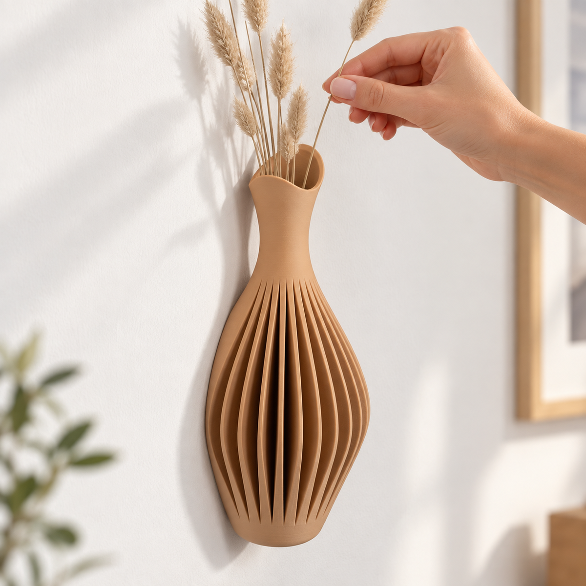 Una mano dispone uno stelo secco nel vaso da parete Rilia.